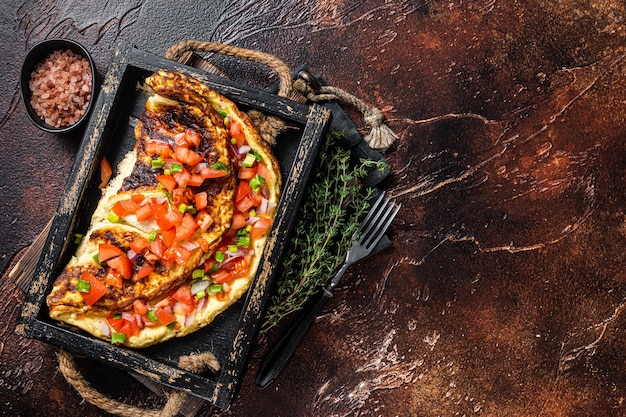 Tortilla de huevos revueltos con tomate, pimiento morrón y cebolla. Fondo oscuro. Vista superior. Copie el espacio.