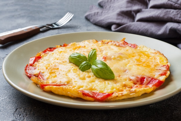 Tortilla, huevos revueltos con tomate y queso en un plato sobre una mesa oscura.