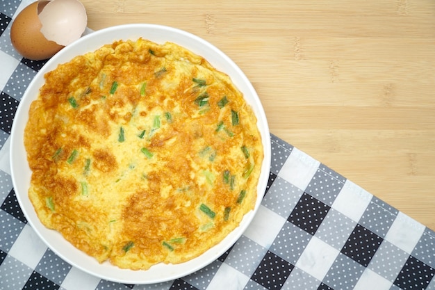 Tortilla de huevos (tortilla, revueltos) con cebolla verde servido en la mesa de madera.