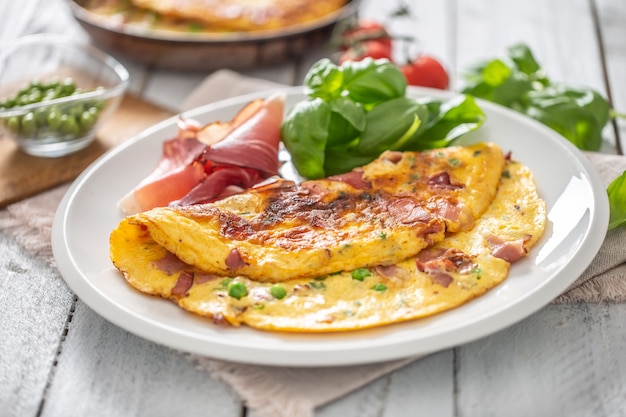 Tortilla con jamón, guisantes, tomates, albahaca y hierbas en un plato blanco.