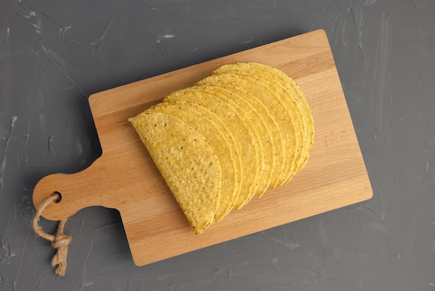 Tortilla de maíz mexicana del ingrediente de las conchas de taco vacías en la tabla de cortar de madera en fondo gris oscuro