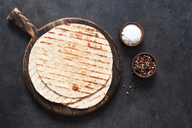 Tortilla a la plancha con especias. Pan plano mexicano - tortilla en una tabla de madera sobre un fondo de hormigón negro.