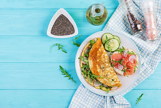 Tortilla con rábano, rúcula verde y sandwich con salmón en plato blanco