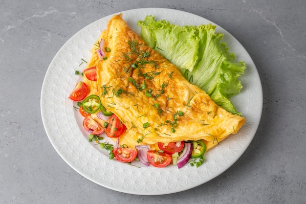 Tortilla rellena casera en un plato. Tortilla de huevo rellena de tomates frescos, queso y perejil verde. Receta de desayuno vegetariano saludable.
