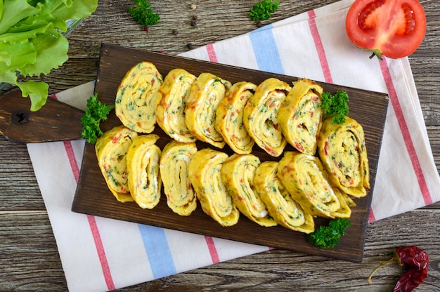 Foto tortilla, rollo de huevo con verduras y hierbas en una mesa de madera. delicioso desayuno saludable. vista superior.