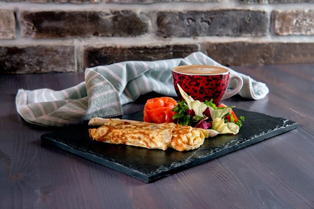 Tortilla con salmón en plato de pizarra y taza de café con leche