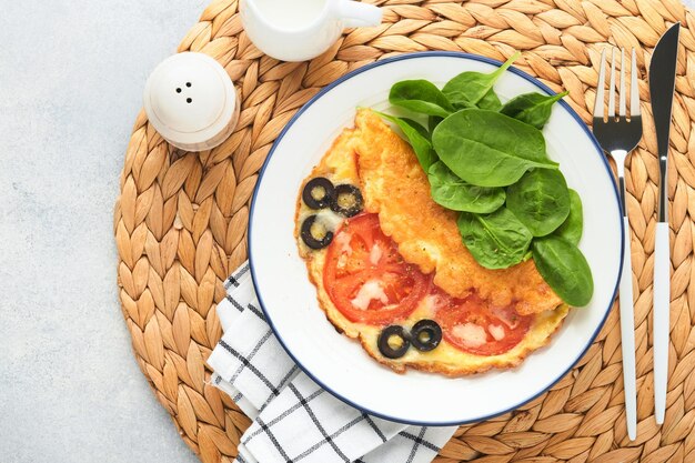 Tortilla con tomates, aceitunas negras, requesón y hierbas de espinacas verdes en un plato blanco sobre fondo de hormigón gris Delicioso desayuno Comida saludable para el desayuno Vista superior