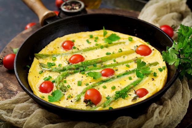 Tortilla (tortilla) con tomates, espárragos y cebollas verdes en sartén.