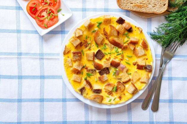 Tortilla con trozos de pan y queso en un plato con cubiertos sobre un mantel a cuadros