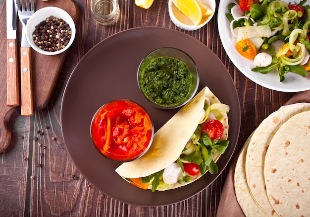 Tortilla vegana mexicana embrulhe pão achatado com legumes e molhos na mesa de jantar