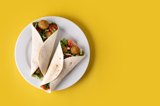 Tortilla-Wrap mit Falafel und Gemüse auf gelbem Hintergrund