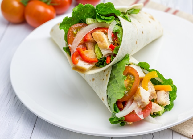 Tortilla Wraps mit gebratenem Hähnchenfilet, frischem Gemüse und Sauce auf weißem Teller