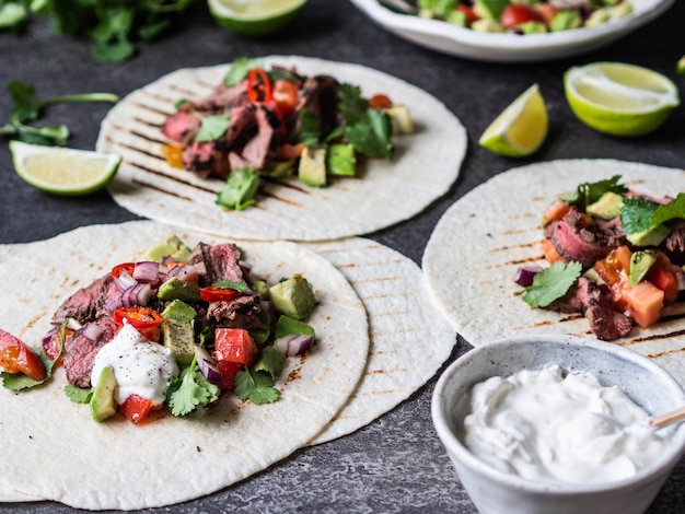 Tortillas mit Gemüse und Rindfleischsteakscheiben. Avocados, Tomaten, rote Zwiebeln und Koriander-Limetten-Saft in Tortillas. Mexikanische Nahrung.