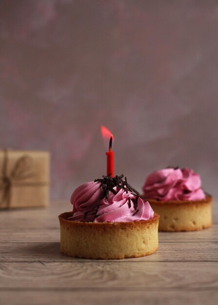 Tortinha redonda doce com creme rosa e chocolate com uma vela em um fundo rosa