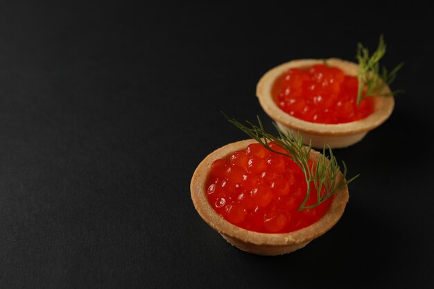 Tortinhas com caviar em fundo preto, espaço para texto