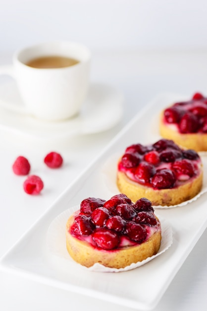 Tortinhas com framboesas e uma xícara de café em um prato branco.