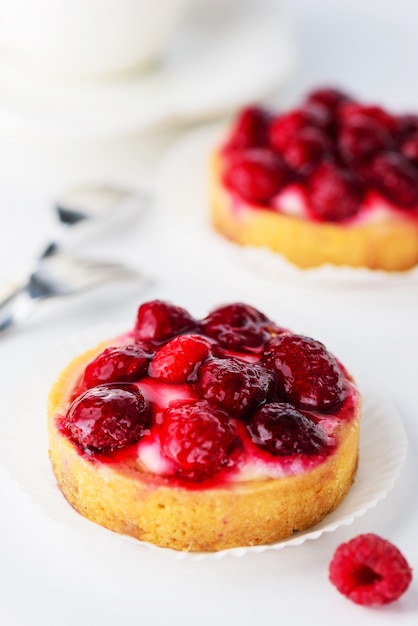 Tortinhas com framboesas e uma xícara de café em uma mesa branca.