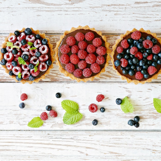 Tortinhas de framboesa e mirtilo com ganache de chocolate, frutas frescas e folhas de hortelã, foco seletivo.