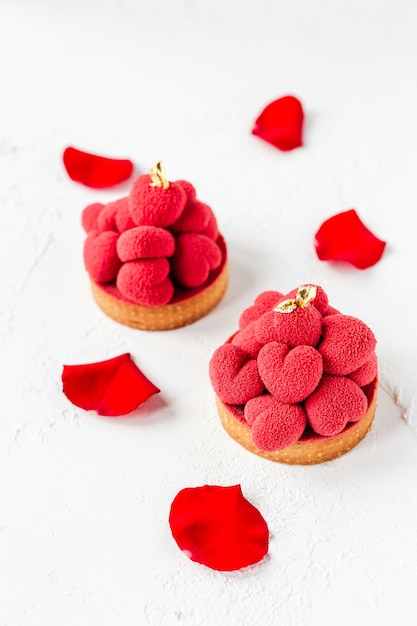 Tortinhas doces de sobremesa com corações de mousse vermelha no topo, decoradas com pétalas de rosa vermelha