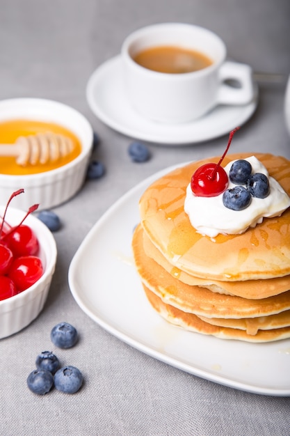 Tortitas con arándanos, cerezas, crema agria, miel y café.