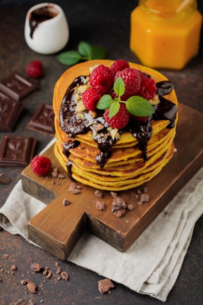 Tortitas de calabaza con frambuesas frescas, chocolate y nueces sobre piedra oscura u hormigón.