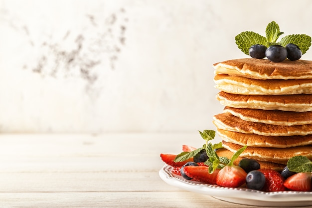 Tortitas caseras con bayas y frutas sobre una superficie blanca