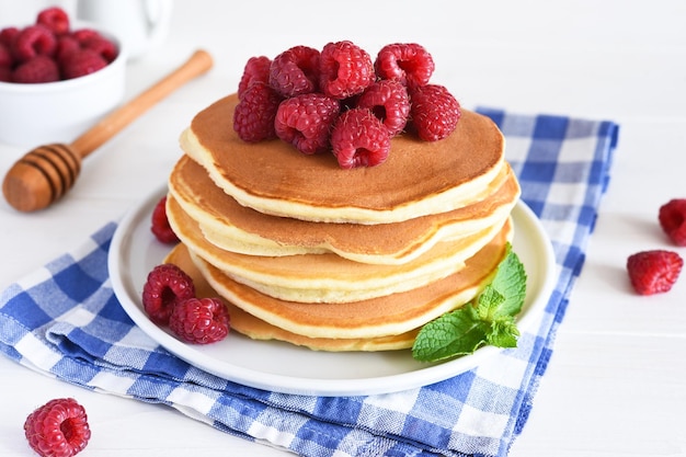 Tortitas caseras con frambuesas y mermelada para el desayuno sobre un fondo blanco.