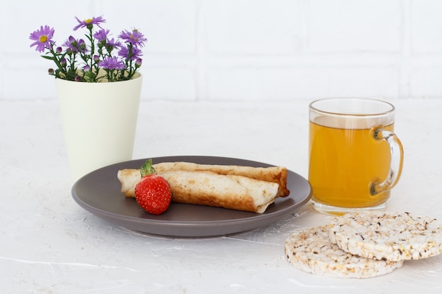 Tortitas caseras rellenas de requesón, una fresa en un plato con una taza de té y flores.