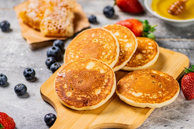 Tortitas caseras en una tabla para cortar con miel y bayas