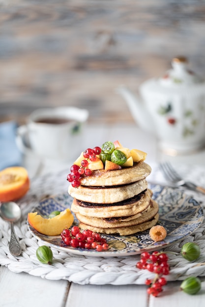 Tortitas de harina de maíz con miel, servidas con bayas y frutas sobre un fondo blanco de madera.