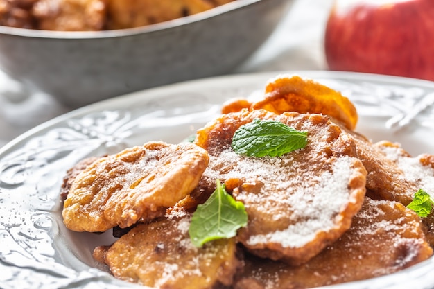 Tortitas de manzana finamente fritas espolvoreadas con azúcar de vainilla y canela cubiertas con hojas de menta.