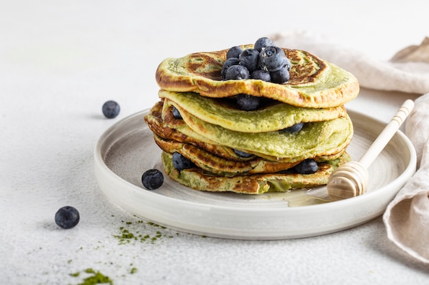 Tortitas de matcha en una mesa blanca con arándanos y miel comida vegana