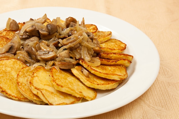 Tortitas de patata con champiñones en el plato en restaurante.