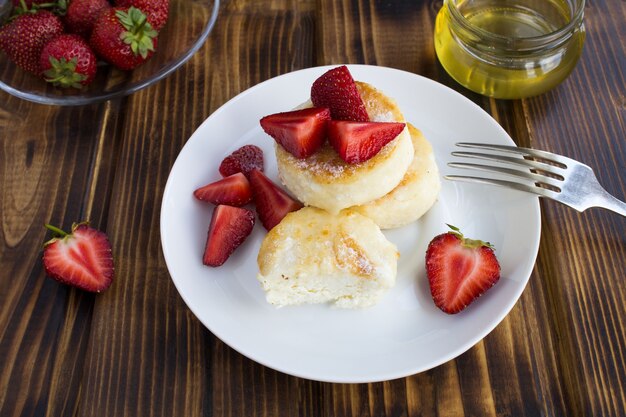 Tortitas de queso, fresas y miel sobre el fondo de madera marrón. De cerca.