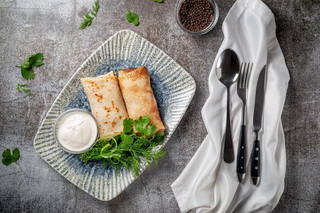 Tortitas rellenas en un plato con perejil y hojas de eneldo y crema agria sobre una mesa de piedra gris