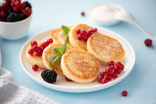 Tortitas de requesón con bayas y crema agria sobre una mesa azul