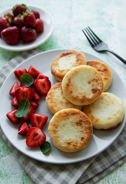 Tortitas de requesón, buñuelos de ricotta en placa de cerámica con fresa fresca. Desayuno saludable y delicioso por la mañana.