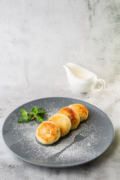 Tortitas de requesón, Syrniki o Cheesecakes con crema, miel, menta aislado sobre fondo de mármol blanco. Comida hecha en casa. Desayuno sabroso Enfoque selectivo. Foto vertical.