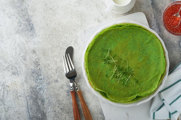 Tortitas verdes Tortitas de crepe de espinacas verdes redondas y delgadas con caviar rojo y negro y salsa de yogur sobre fondo de hormigón gris Desayuno vegano saludable Día Nacional de Panqueques o Día del Martes Gordo