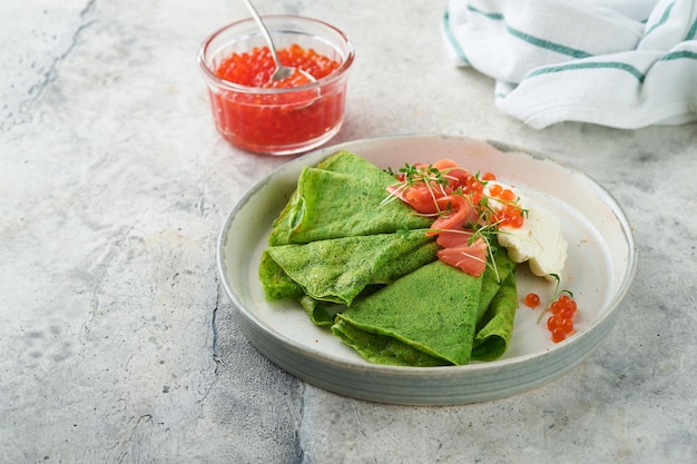 Tortitas verdes Tortitas de crepe de espinacas verdes redondas y delgadas con caviar rojo y negro y salsa de yogur sobre fondo de hormigón gris Desayuno vegano saludable Día Nacional de Panqueques o Día del Martes Gordo