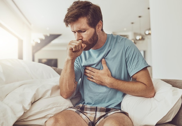 Foto tos enfermo y hombre en un sofá con dolor en el pecho tuberculosis o gripe en casa asma ansiedad y persona masculina con dificultad para respirar en la sala de estar con neumonía covid o virus pulmonar