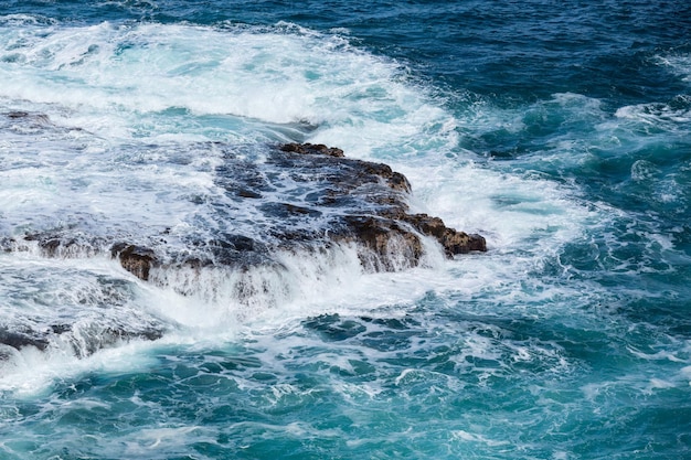 Tosendes Meer fließt über Lavafelsen an der Küstenlinie