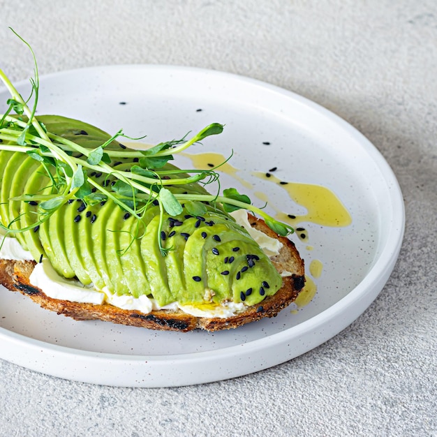 Tostada de aguacate integral con queso crema, semillas de sésamo negro, aceite de oliva y microvegetales