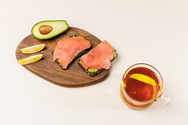 Tostada de aguacate con pan guacamole salmón ahumado y semillas de sésamo Cerca de una taza de té Desayuno saludable