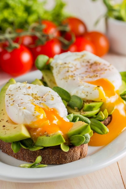 Tostada del aguacate, tomate de cereza y huevos escalfados en fondo de madera.