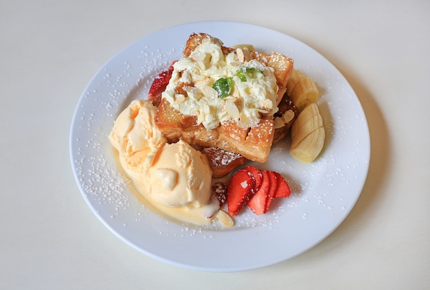 Tostada de miel servida con fruta plátano y fresa y helado en plato blanco.