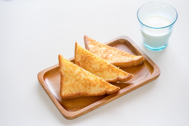 Tostada de queso crujiente en placa de madera sobre fondo blanco con leche en vaso