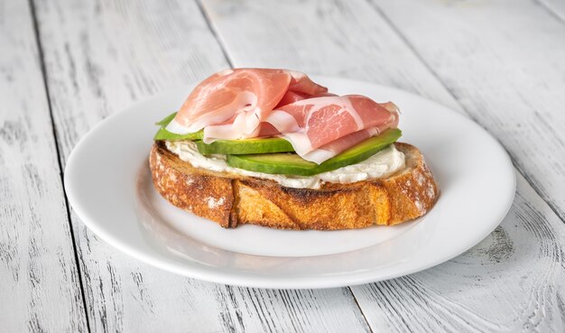 Tostada con rodajas de aguacate, prosciutto y queso crema