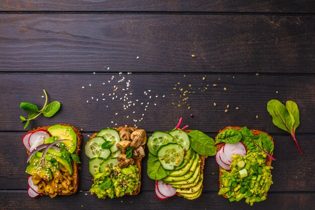 Tostadas de aguacate con diferentes ingredientes, vista superior, fondo de madera oscuro, espacio de copia.