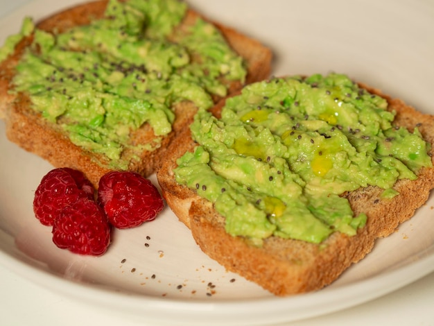 Tostadas con aguacate y frambuesas en un plato blanco desayuno saludable dieta comida vegetariana concepto de comida vegetariana vegetariana